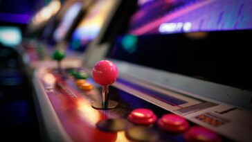 Close-up of a colorful vintage arcade machine with glowing joysticks and buttons in a dimly lit game room.