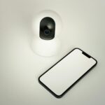 A smart home security camera paired with a blank smartphone on a white background.