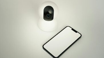 A smart home security camera paired with a blank smartphone on a white background.
