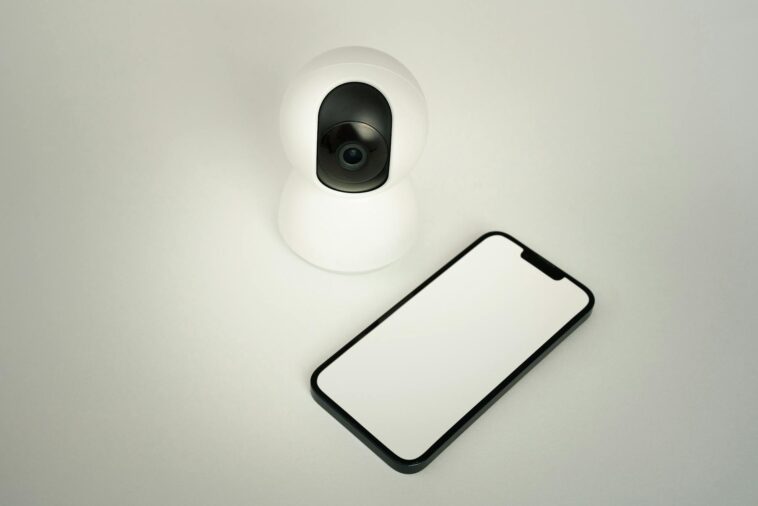 A smart home security camera paired with a blank smartphone on a white background.