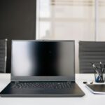 A sleek office setup featuring a laptop, notebooks, and chairs on a white desk.