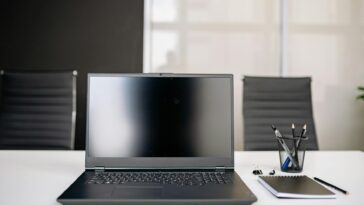 A sleek office setup featuring a laptop, notebooks, and chairs on a white desk.