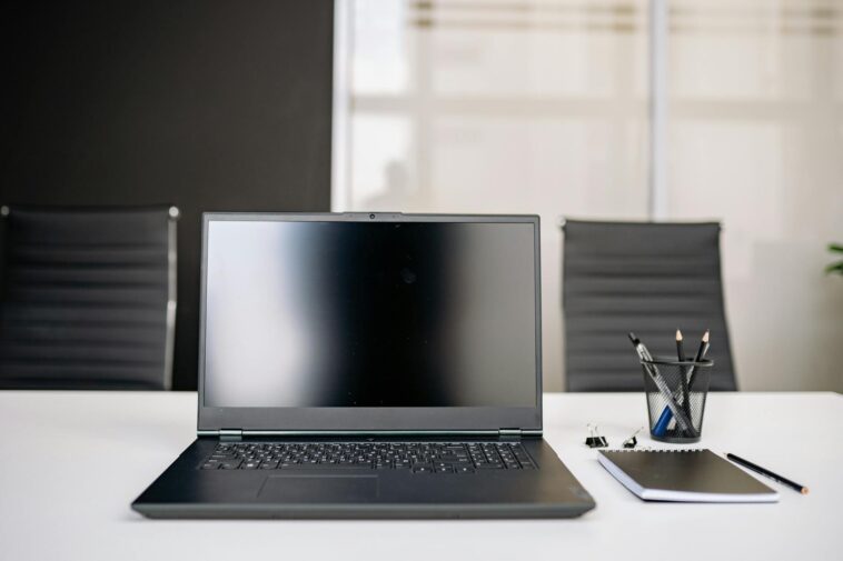 A sleek office setup featuring a laptop, notebooks, and chairs on a white desk.