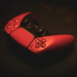 Close-up of a pink gaming controller, highlighting its sleek design in a dark, moody setting.