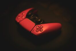 Close-up of a pink gaming controller, highlighting its sleek design in a dark, moody setting.
