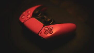 Close-up of a pink gaming controller, highlighting its sleek design in a dark, moody setting.