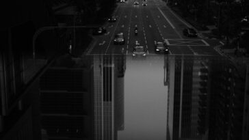A striking black and white image of a busy urban street with modern skyscrapers and vehicles in motion.