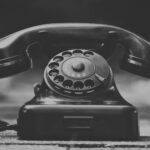Close-up of a classic black rotary telephone with blurred background, in grayscale.