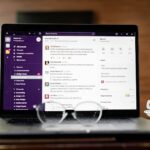 Laptop displaying a messaging app, with eyeglasses and coffee cup on a wooden table.
