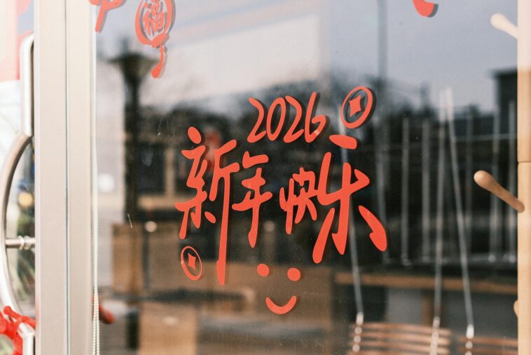 Red Chinese characters with 2026 on a glass door, symbolizing New Year celebrations.