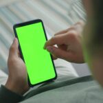 Close-up of a person using a smartphone with a green screen indoors.