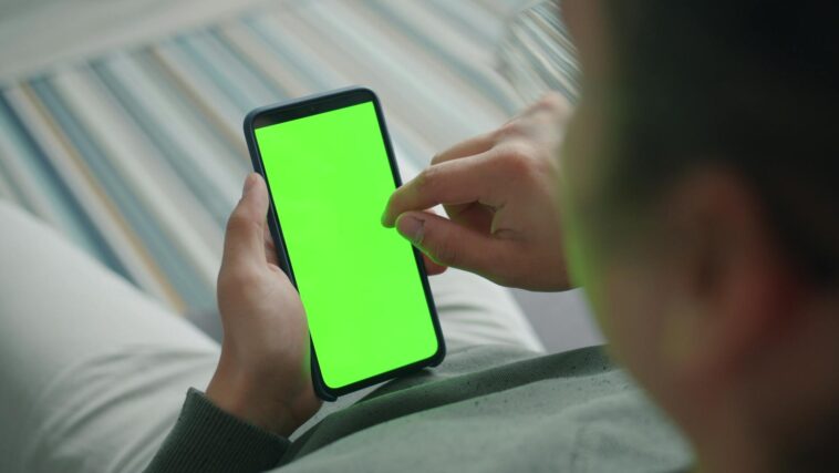 Close-up of a person using a smartphone with a green screen indoors.