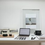 Modern laptop with blank screen arranged with retro filmstrips photo camera and framed picture placed on table near coffee and stack of books