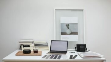 Modern laptop with blank screen arranged with retro filmstrips photo camera and framed picture placed on table near coffee and stack of books