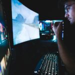 A man in eyeglasses focused on multiple screens, showcasing modern technology setup.