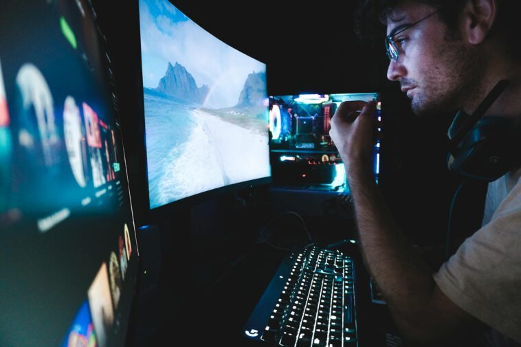 A man in eyeglasses focused on multiple screens, showcasing modern technology setup.