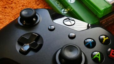 Xbox controller close-up with game cases on orange background.