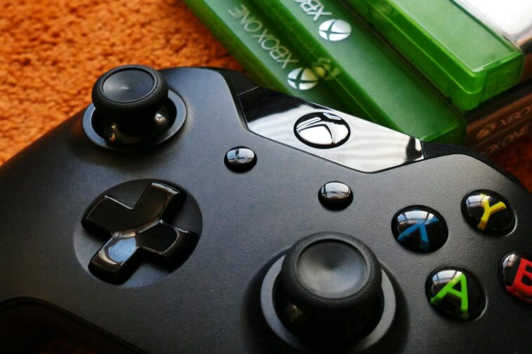 Xbox controller close-up with game cases on orange background.