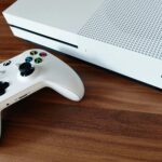 Close-up of a white Xbox console and controller on a wooden surface, ideal for gaming enthusiasts.