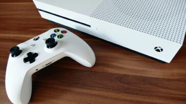 Close-up of a white Xbox console and controller on a wooden surface, ideal for gaming enthusiasts.